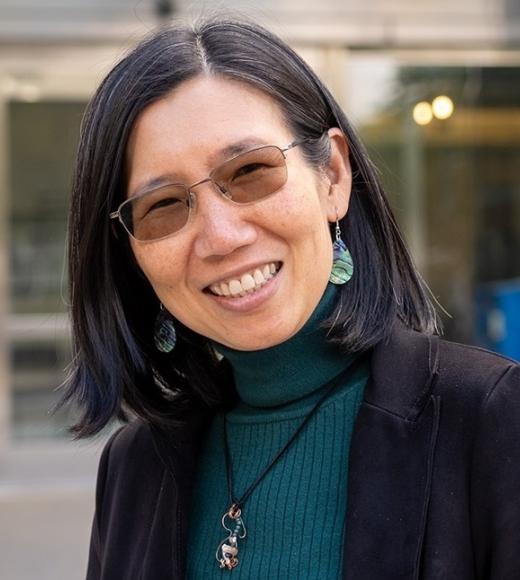 Smiling headshot of Asian woman in glasses, teal turtleneck and turquoise earrings
